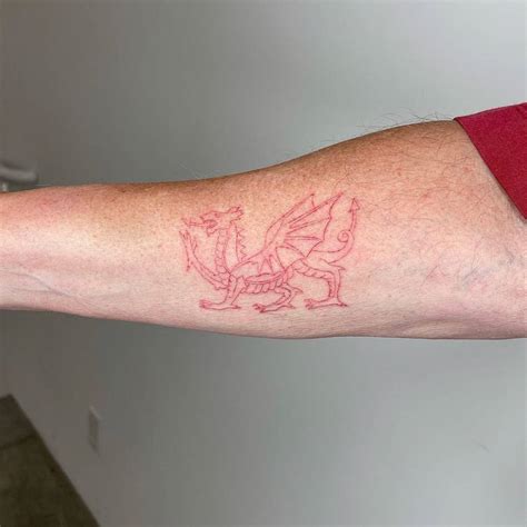 FIne line red Welsh Dragon tattoo on the inner forearm.