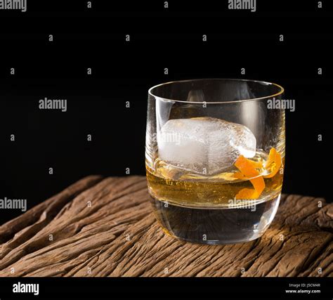 Glass of Scotch whisky on an old rustic wooden background. Modern styling with one large ice ...