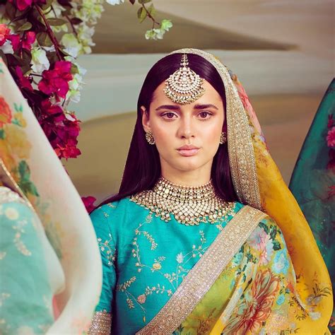 a woman in a green and yellow outfit with jewelry on her head standing next to flowers