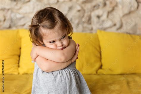 Pouting little girl with crossed arms on yellow couch Stock Photo | Adobe Stock