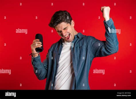 Man smiling, dancing with wireless portable speaker in studio on red ...