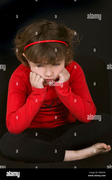 little girl pouting with face resting on hands against black background Stock Photo - Alamy