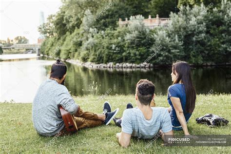 Three people relaxing in park with guitar — male, sitting - Stock Photo | #199984052