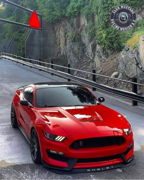 a red sports car parked on the side of a road near a cliff and bridge