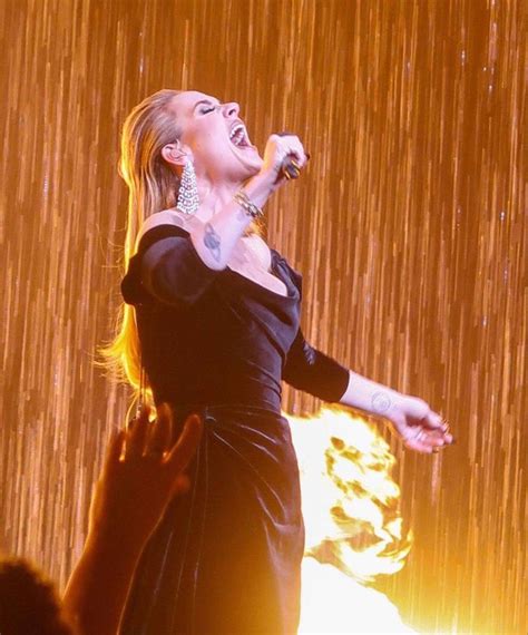 a woman in a black dress singing on stage with her hands out to the side