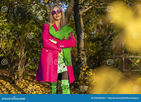 Beautiful Woman Wearing a Pink Elegant Coat and Green Scarf is Posing Outdoors on a Sunny Autumn ...