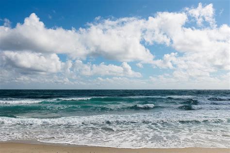 Ocean washing up onto a beach with cumulus clouds in the sky ...