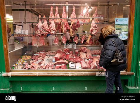 Meat hangs on display in a traditional butchers shop window with a woman looking on Stock Photo ...