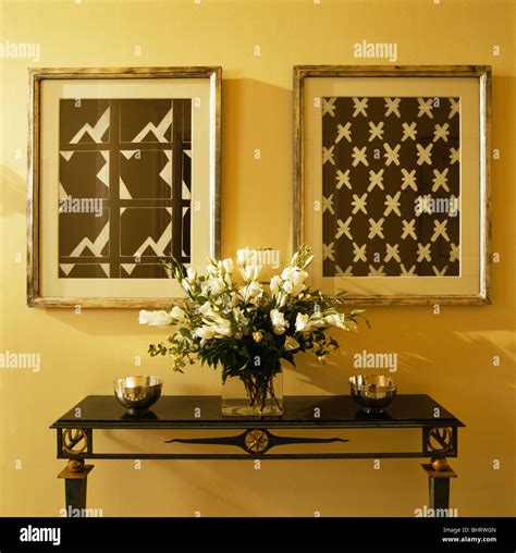 Black+white abstract pictures above vase of white flowers on console ...