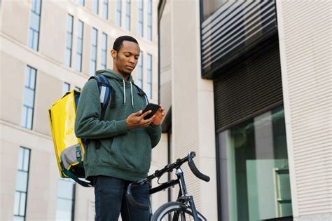 Premium Photo | A bicycle courier with a yellow backpack looks at the phone screen against the ...