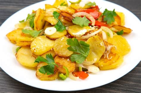 Premium Photo | Cooked fried potatoes with herbs and vegetables in a white plate on a wooden table