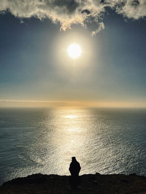 Premium Photo | A person is sitting on a cliff overlooking the ocean at ...