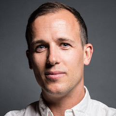 A studio portrait of a clean-shaven light-skinned man with short dark hair in a white shirt.