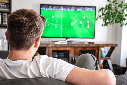 Young man watching soccer game on TV sitting on a couch at home