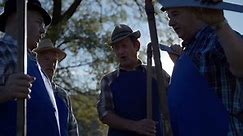 Farmers singing at the brake from mowing the grass with scythes. Close up slow motion of a local farmers standing in circle and singing at brake from mowing with scythes in countryside on sunny day.