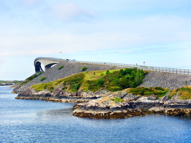 A large concrete road bridge rising over a small body of land and blue  water