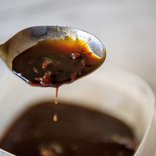 A dark Sweet soy glaze drips off the end of a spoon.