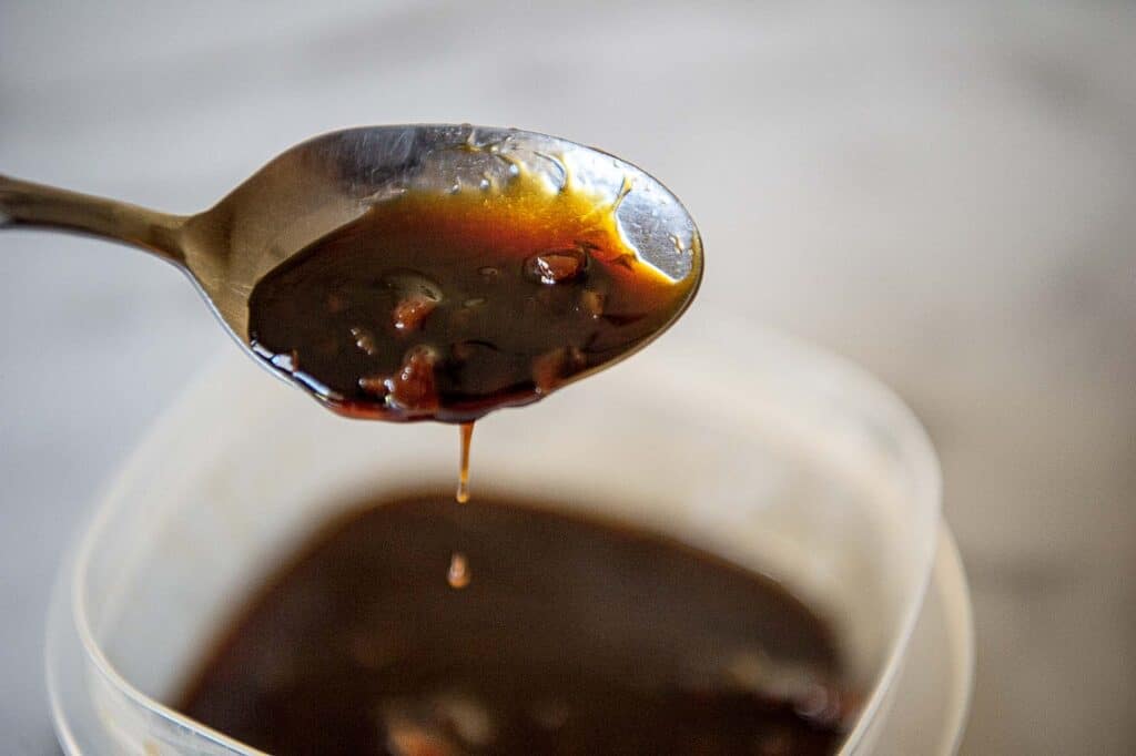 A dark Sweet soy glaze drips off the end of a spoon.