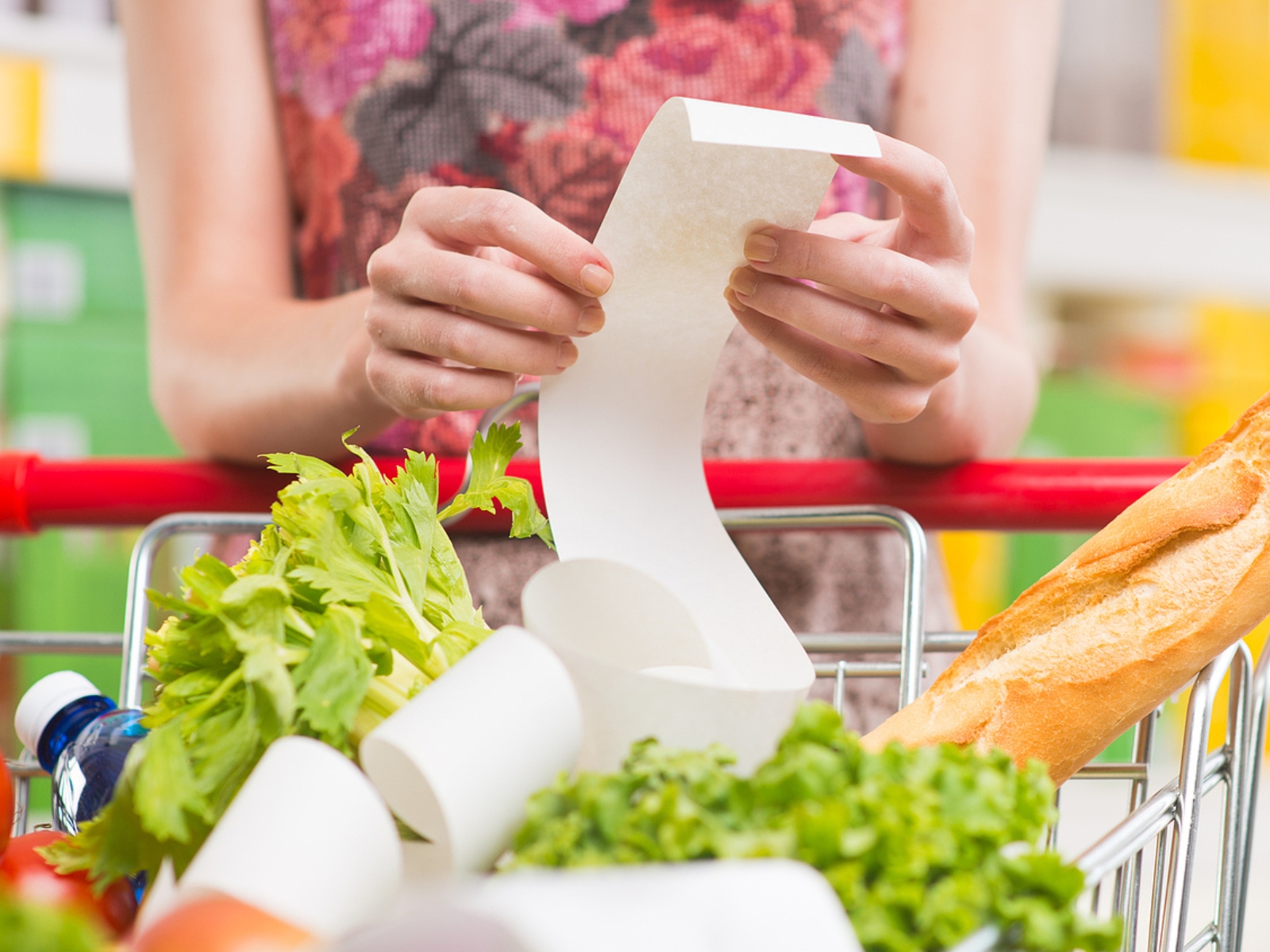 woman's hands holding receipt over cart of groceries