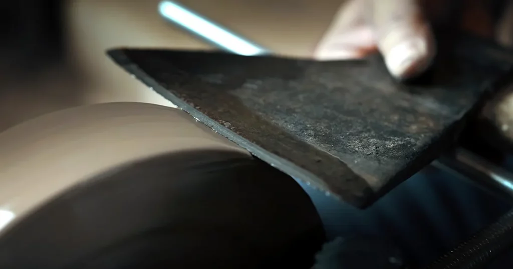 Asian man sharpening axe on a grinder