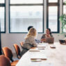 Four professionals discuss operations and train in a conference room using a tablet and a laptop.