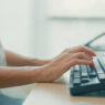 A person works at a desk, typing on a keyboard.