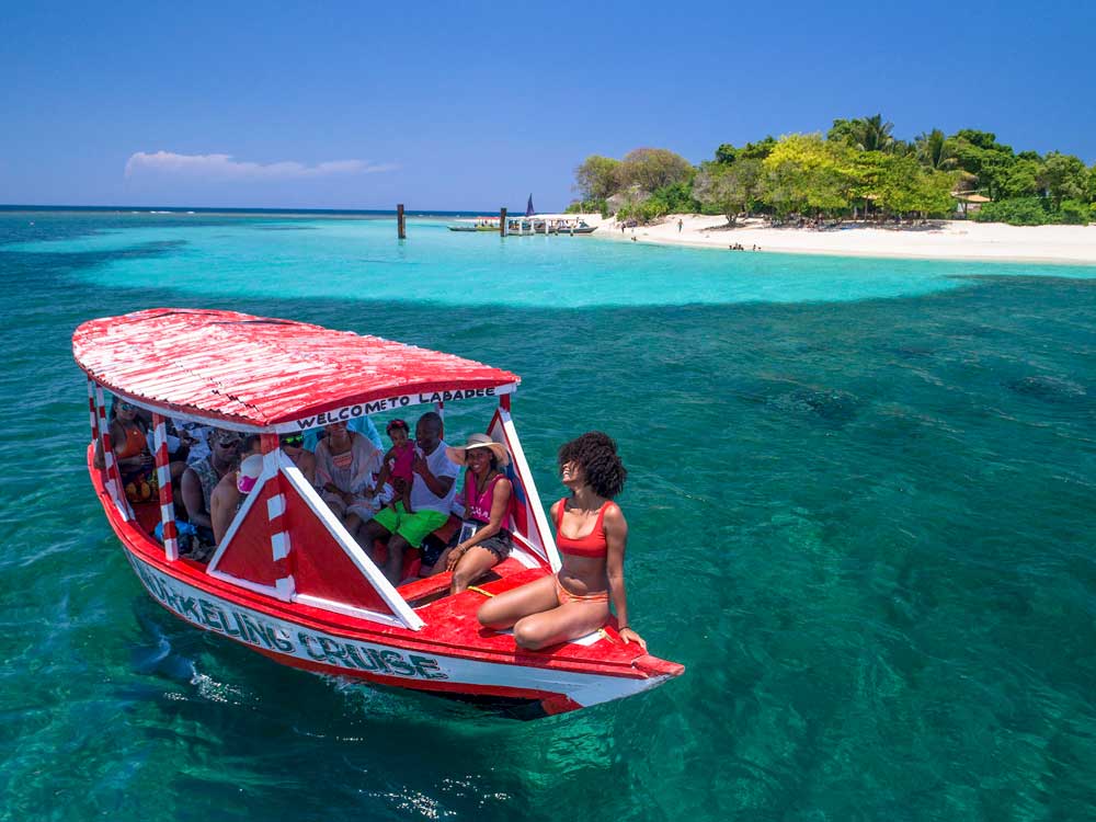 A group of people on a red boat in clear turquoise waters near a tropical island.