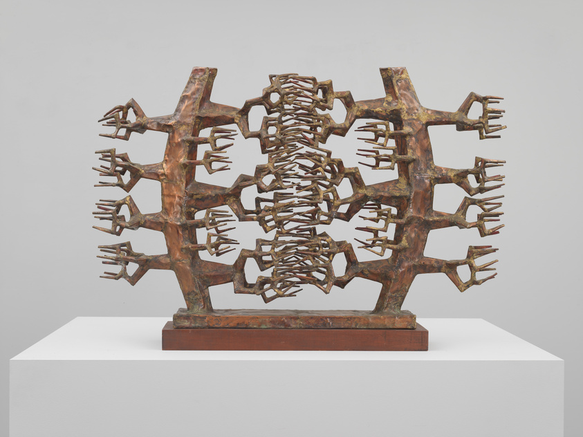 A complex bronze sculpture resembling a tree with an intricate lattice of branches displayed on a white pedestal against a neutral background.