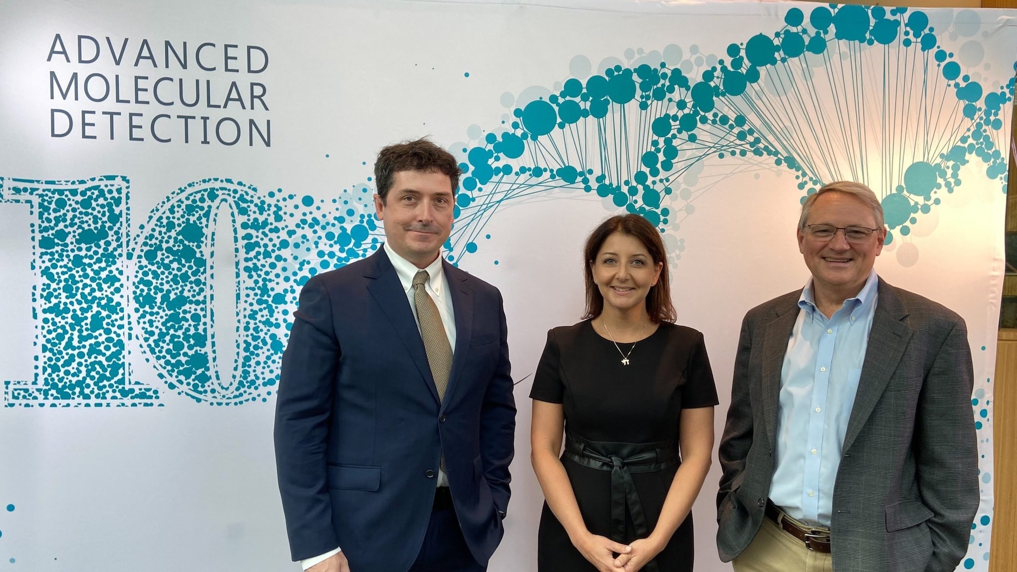 Photo of a woman and two men standing in front of a poster that says Advanced Molecular Detection