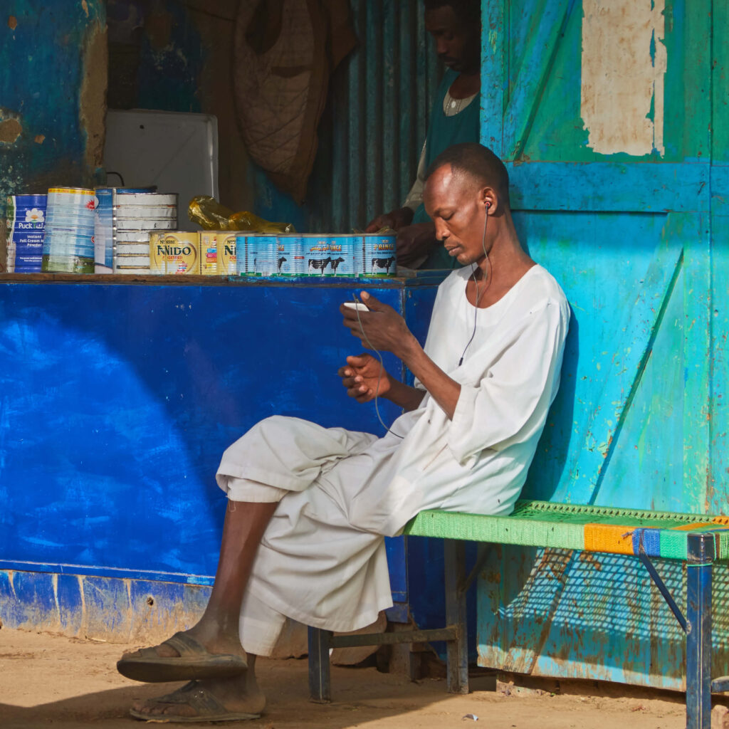 Man with phone and earbuds sitos outside vendor