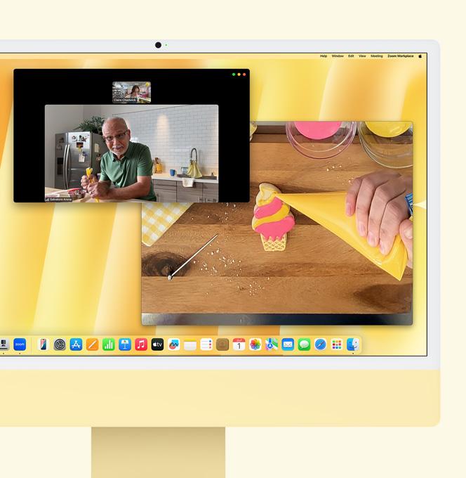 iMac باللون الأصفر. عرض توضيحي لميزة العرض الرأسي. شاشة تعرض صانعة حلويات تشارك في مكالمة فيديو مع شخص آخر. وتعرض إحدى الشاشتين صانعة الحلويات ووجه الرجل، بينما تعرض الشاشة الأخرى يدي صانعة الحلويات وهي تزيّن قطعة بسكويت