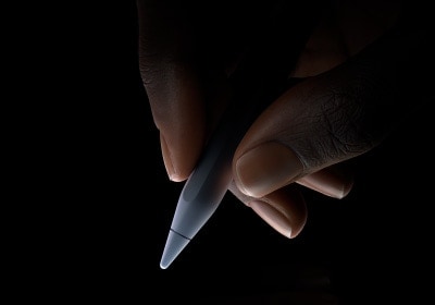 Una mano sostiene un Apple Pencil Pro desde la parte inferior, entre el pulgar y el índice, en posición para escribir.