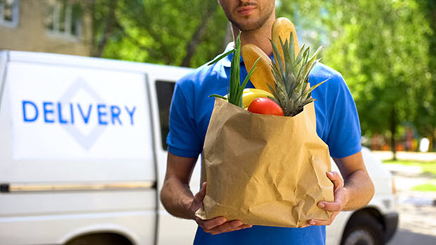 Man in a blue shirt holding a bag of groceries.  A delivery van is seen in the background