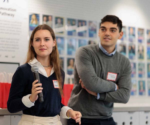 A woman standing giving a presentation with a microphone next to a man