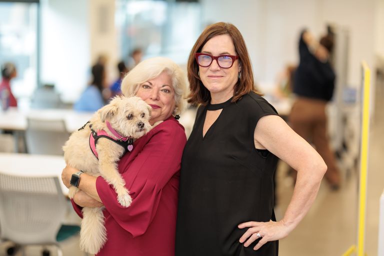 Two women pose for a photo while holding a small dog