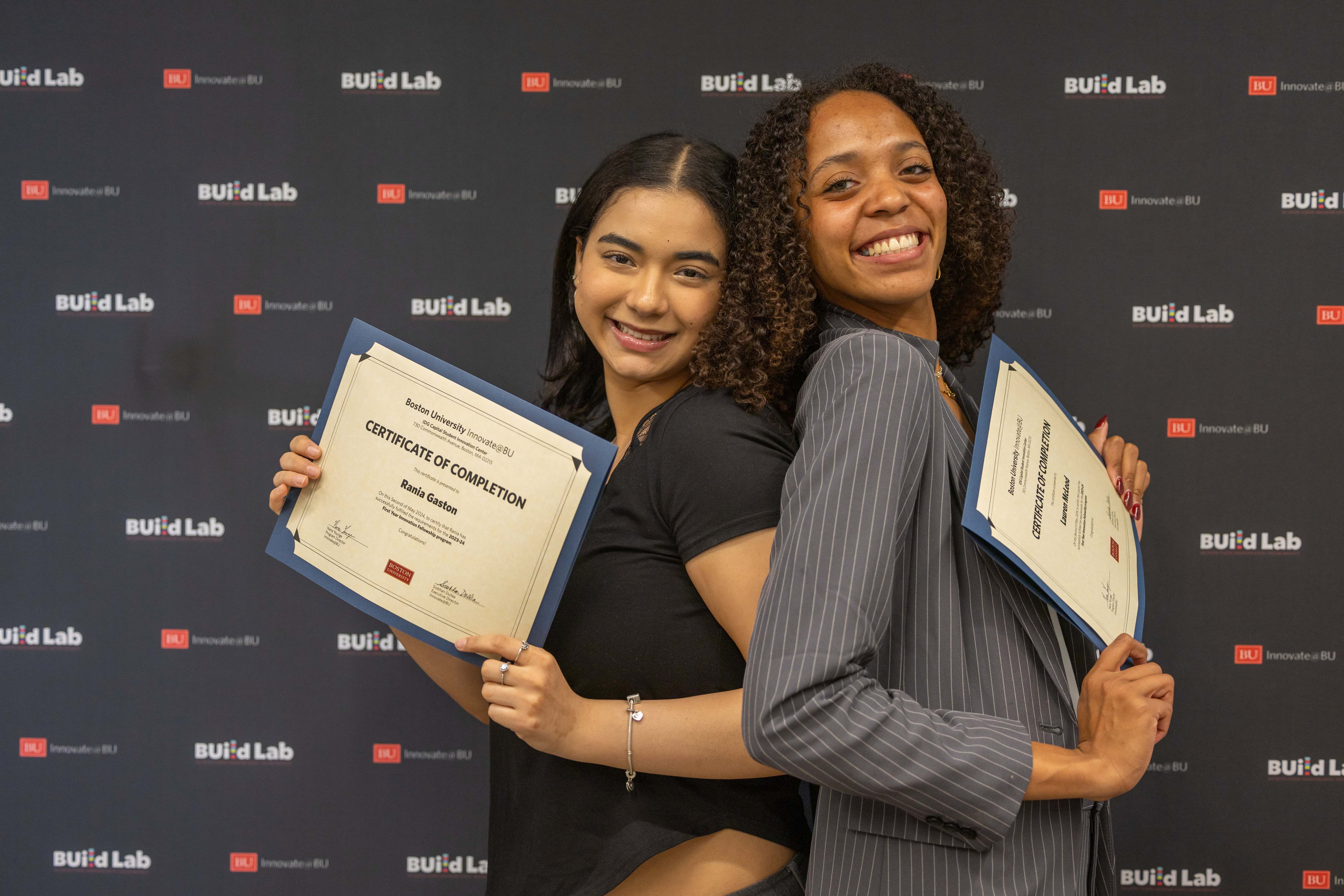 Two women standing with certificates in front of a BU backdrop