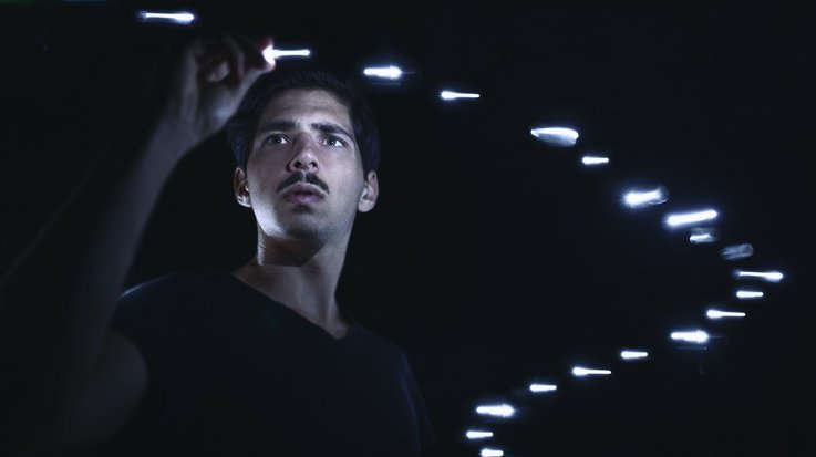 Man surrounded by floating silver bars plucks one from the air with black background