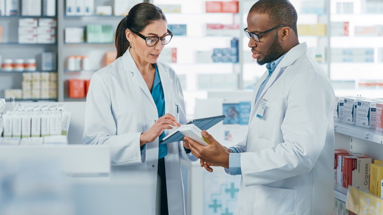 Two pharmacists talk to each other and operate a tablet