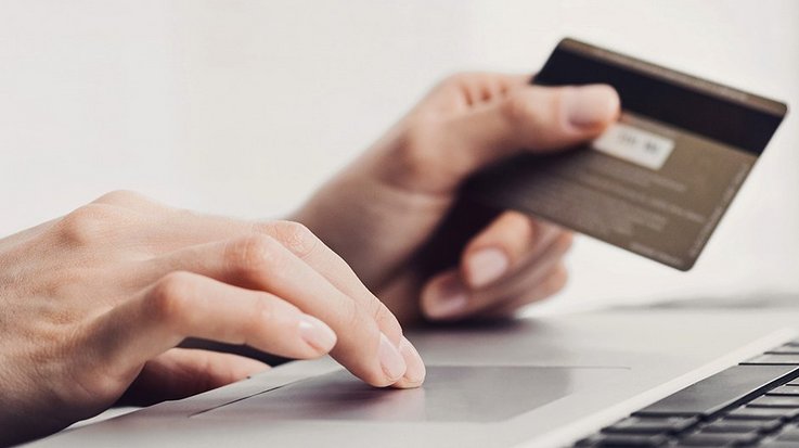 Two hands, one operating the keyboard of a laptop, the other holding a credit card