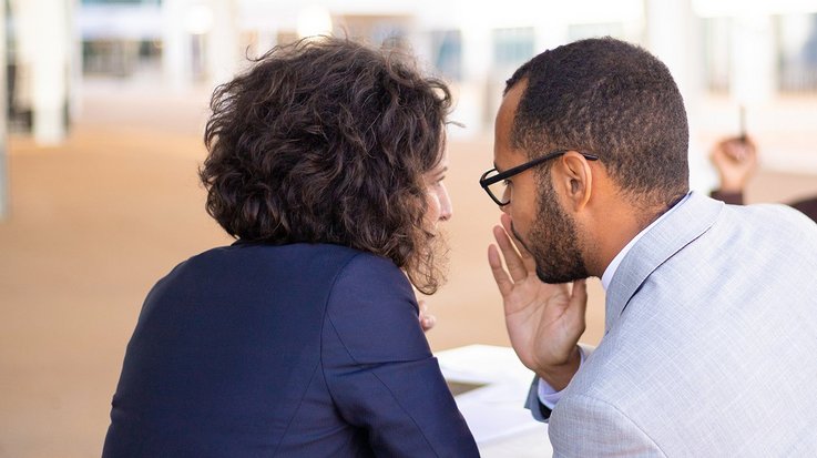 Two colleagues whisper while a third sits a little further away