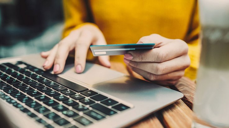 A woman is typing something into her laptop and holding a credit card in the other hand