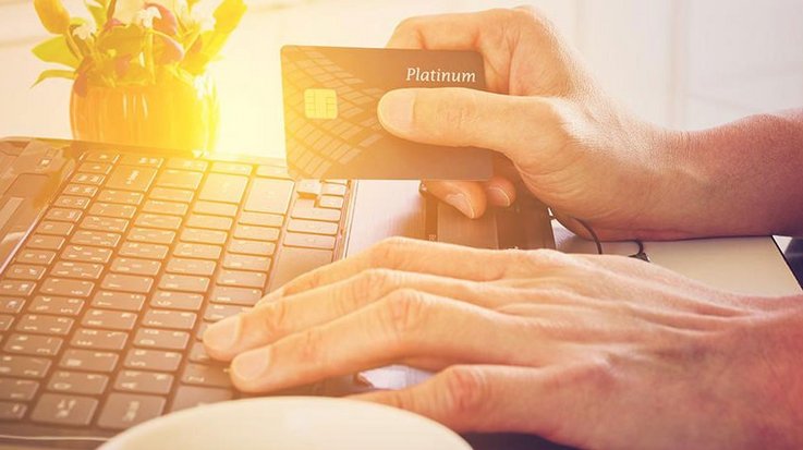 A man has his hands on the keyboard of his laptop and holds a credit card in his hand