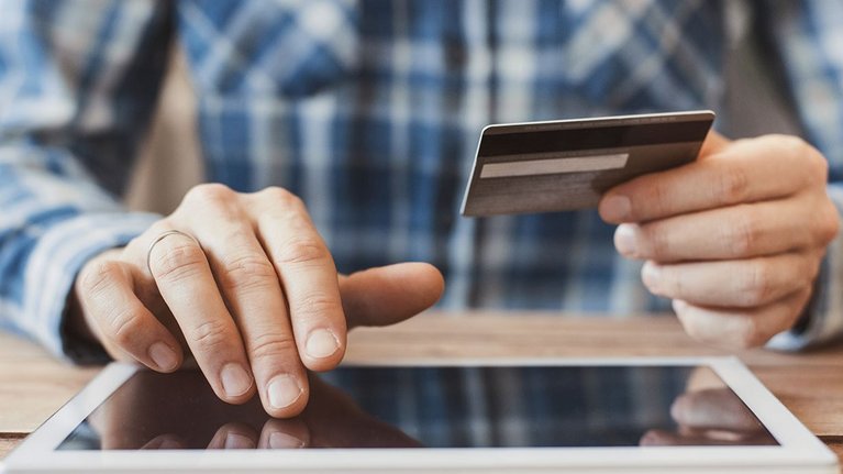 A man operates a tablet and holds a credit card in the other hand