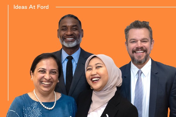 Four individuals, two men and two women, dressed in business casual and formal attire, stand against an orange background with "Ideas At Ford" written in white at the top left. The women are smiling; one wears a hijab. The men are also smiling, both in a suit and tie.