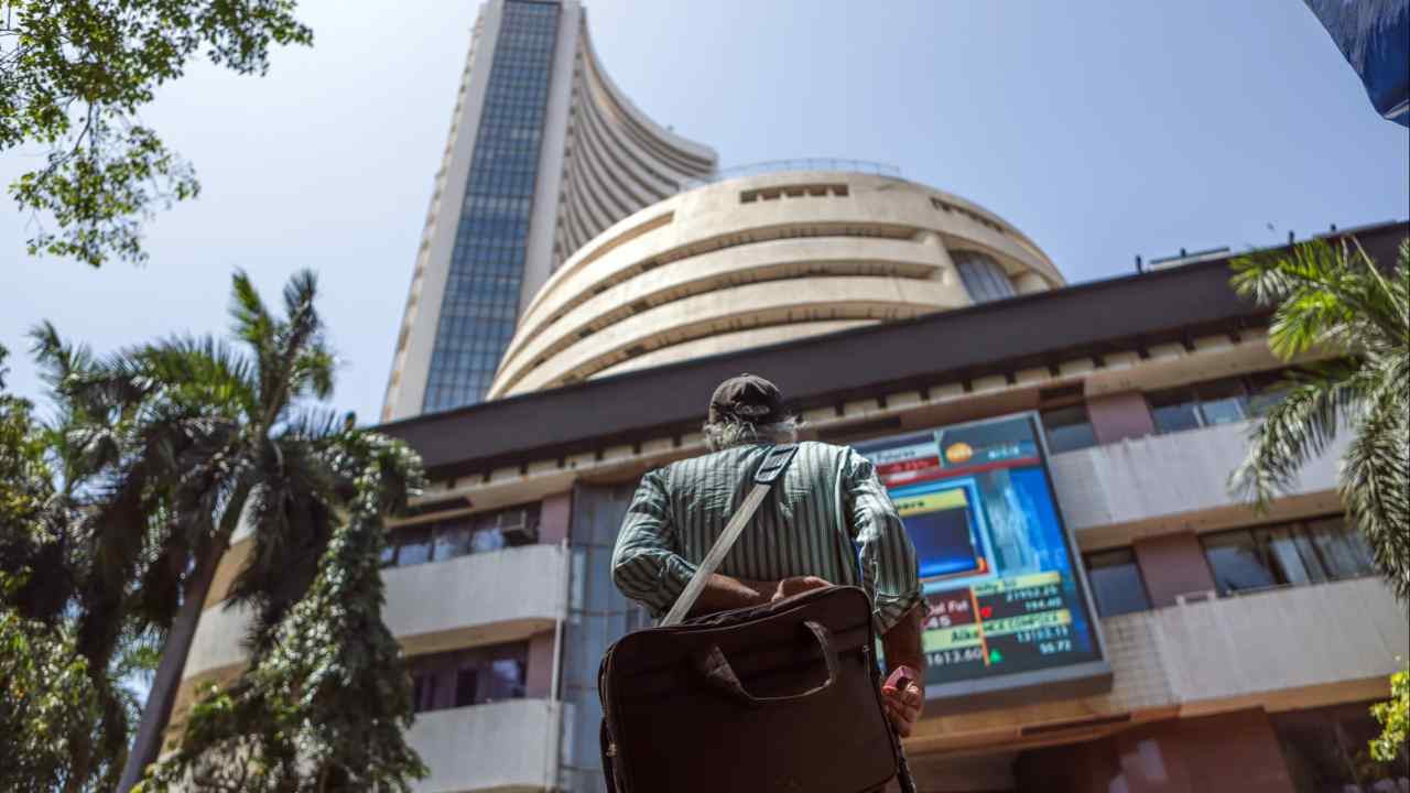 A pedestrian stands outside the Bombay Stock Exchange building in Mumbai, looking up at the building and its electronic display board.