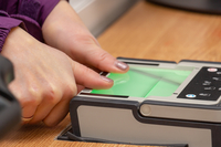 Photo of a person placing both of their thumbs onto a digital fingerprinting machine.