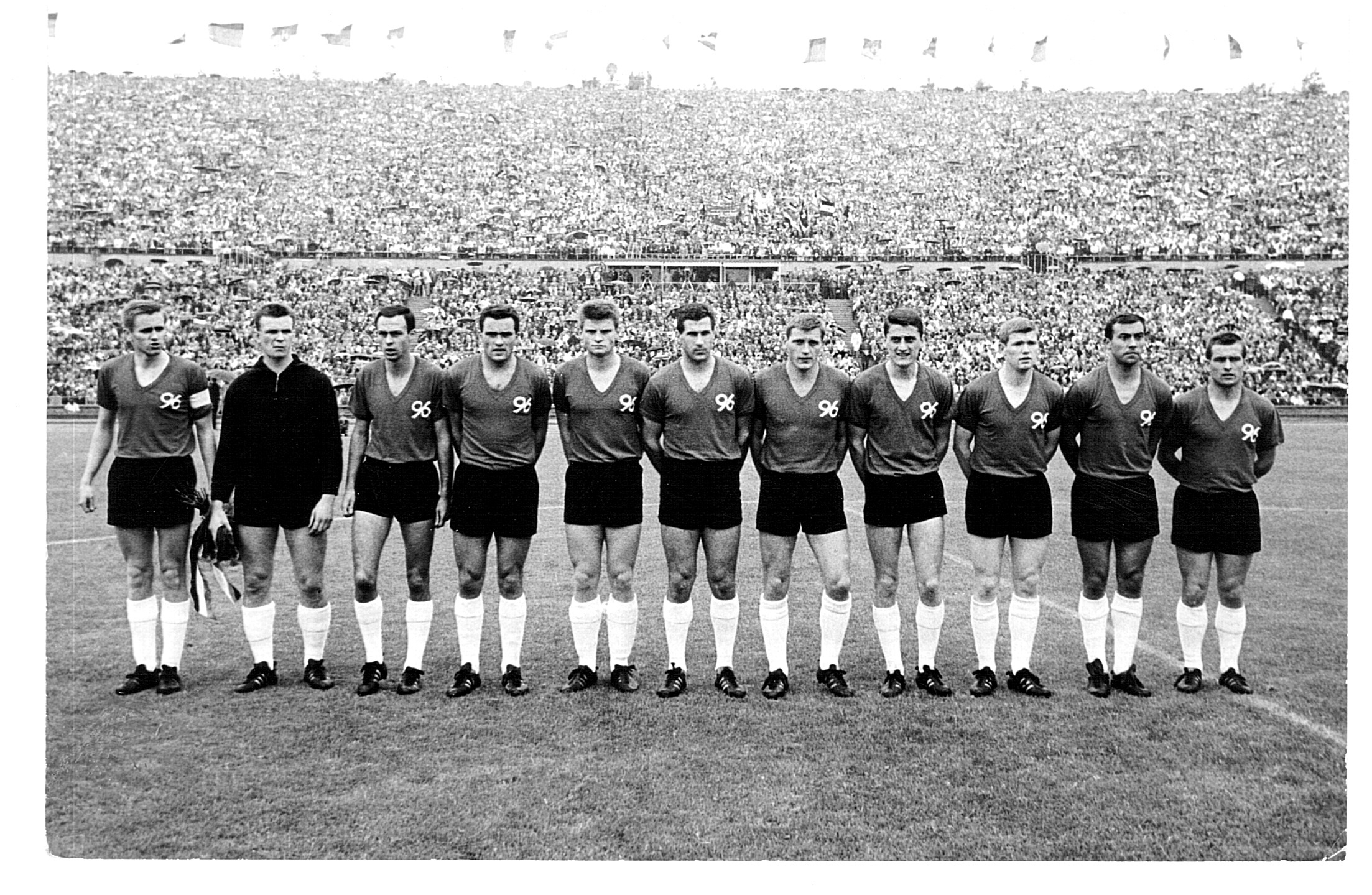 Schwarz-weiß Foto einer Fußballmannschaft in einem vollen Stadion.