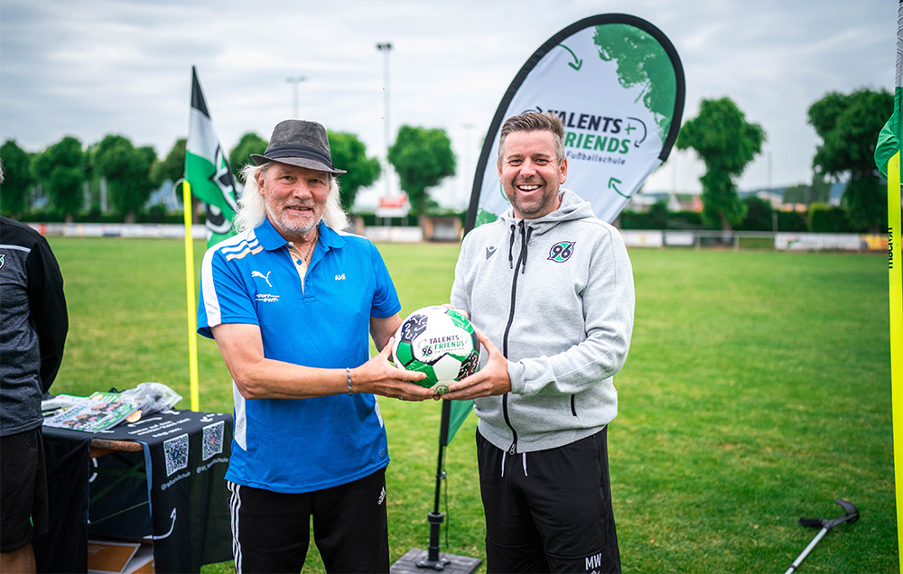 Zwei Männer halten gemeinsam einen Ball in die Kamera.