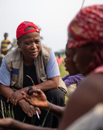 A Mercy Corps staff member crouches to speak to a group of people sitting down.