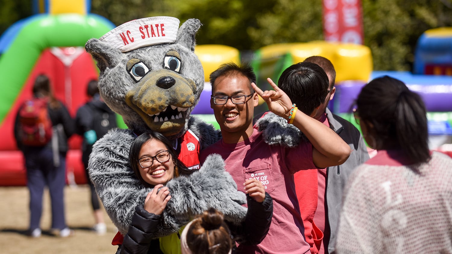 Mr. Wuf hugs two smiling students during the 2019 Day of Giving student event.